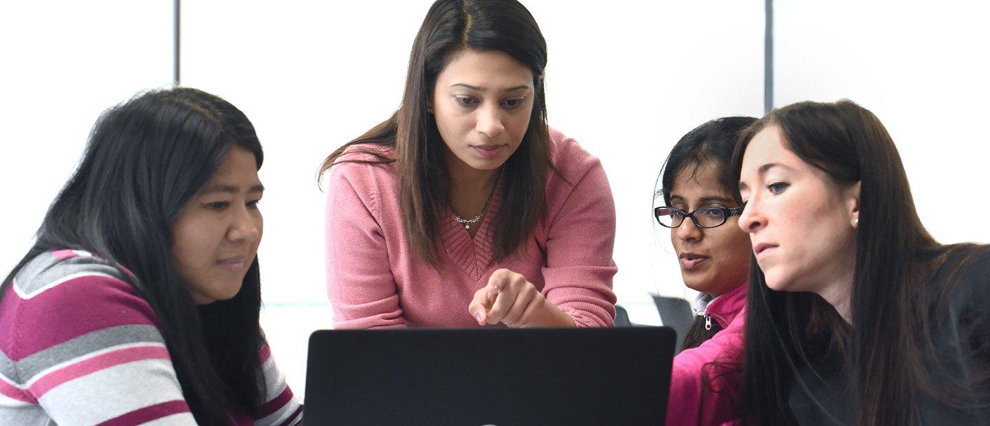 group of women standing around an open laptop, pointing at the screen